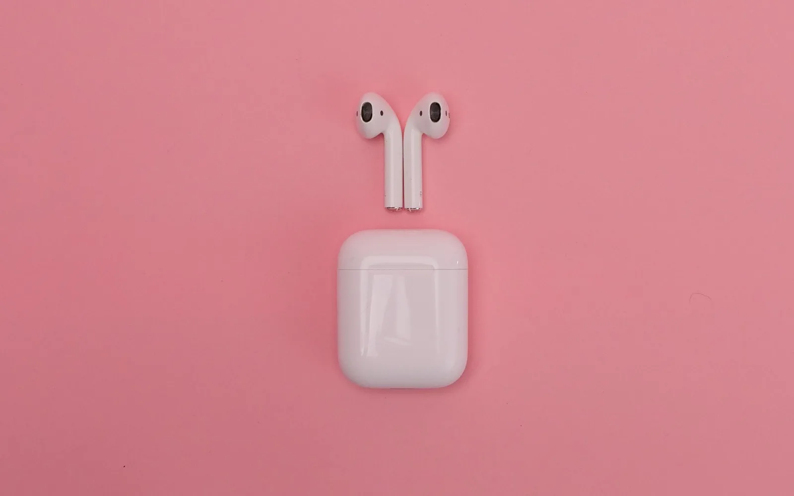 AirPods et boîtier de recharge sur un fond rose, illustration d'écouteurs endommagés par l'eau pour l'assurance